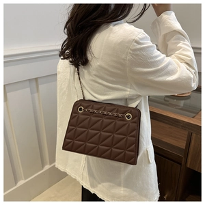 Detail of dark brown quilted chain shoulder bag featuring gold eyelets and leather strap