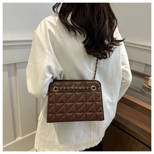 Rear view of model wearing a brown quilted crossbody bag with gold chain strap