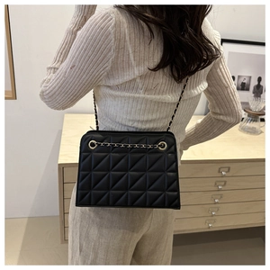 Detail of a black quilted crossbody bag with gold chain strap on a person in indoor setting