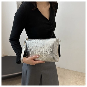 Detail of silver crocodile-patterned clutch bag held by model for modern fashion look