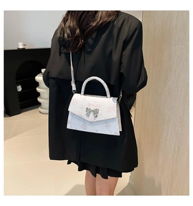 White butterfly print crossbody bag with silver bow lock shown on a model in black blazer
