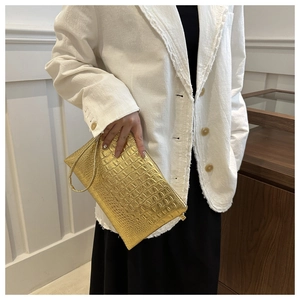 Detail of metallic gold envelope clutch bag with crocodile texture and wristlet strap
