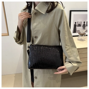 Detail of black faux crocodile leather crossbody bag with wide strap and gold hardware