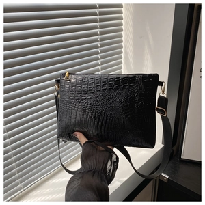 Detail of black faux-crocodile leather shoulder bag with gold hardware in sunlight