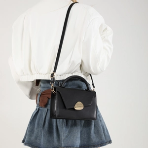 Minimalist black leather handbag with gold metal clasp shown on model in studio