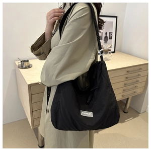 Minimalist black nylon tote bag with large capacity and broad shoulder strap on a model