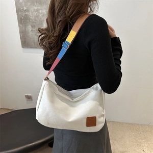 Minimalist white canvas tote bag with a wide colorful patchwork strap and leather label