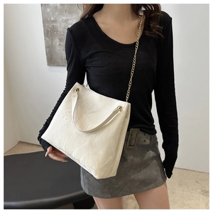 Close-up of cream tote bag with FASHION embossed logo and gold chain strap on shoulder
