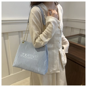 Detail of light blue shoulder bag featuring FASHION embossed texture and gold chain strap