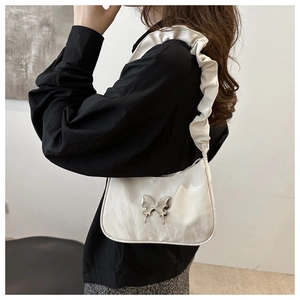 Close-up of white crescent underarm bag with silver butterfly and ruffled strap