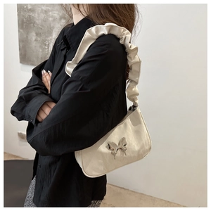 Close-up of stylish off-white crescent bag with metal butterfly and ruched strap