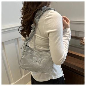 Detail of silver pleated crescent underarm bag with metallic butterfly and drawstring strap