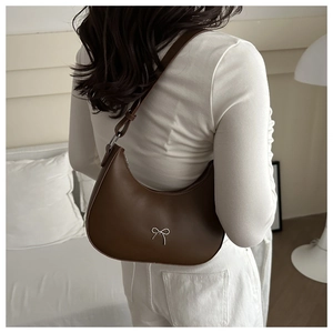 Detail of a brown crescent shoulder bag featuring a decorative silver metallic bow accent