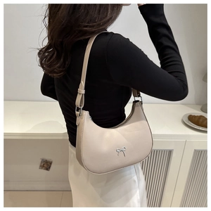 Detailed view of beige hobo bag with silver bow accent worn as an underarm shoulder bag