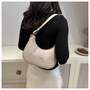 Detail view of cream crescent underarm bag with silver bow accent on model shoulder
