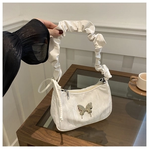 Detailed view of white crescent bag with silver butterfly accent and pleated handle
