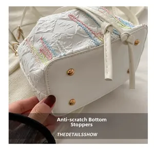 Detail view of white handbag base with colorful stitching and golden metal protective studs
