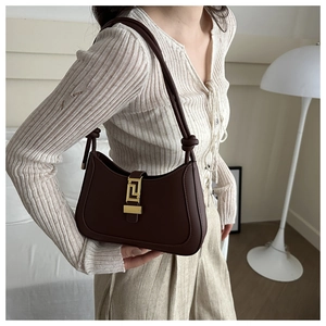 Detail of a dark brown crescent bag with a gold geometric clasp and knotted strap
