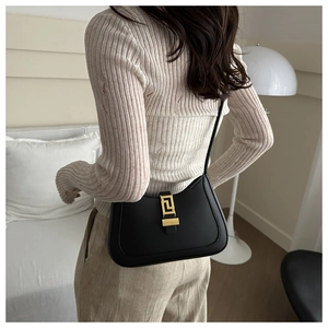 Detail of black crescent shoulder bag featuring a geometric gold buckle and matte leather