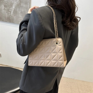 Minimalist beige quilted crossbody bag with gold chain strap shown on a dark blazer