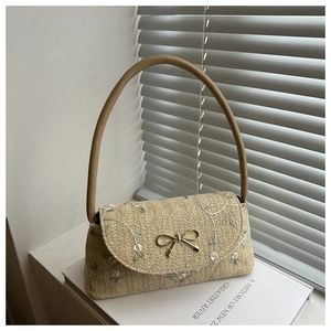 Détail du sac baguette tissé beige avec broderie florale et boucle de nœud dorée