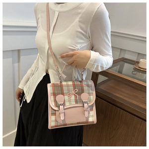 Detail of pink plaid crossbody bag with bow accent and leather straps on model