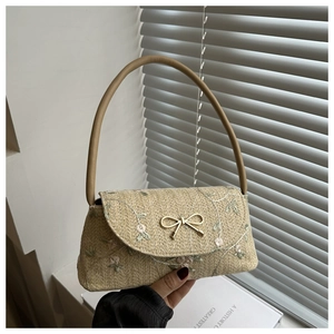 Détail de broderie florale et boucle nœud doré sur un sac baguette en paille