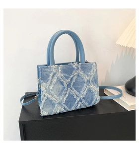 Detail of light blue denim square bag with frayed diamond texture and leather handles