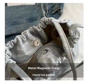 Detail of grey bucket bag showing magnetic hardware closure and pleated opening texture