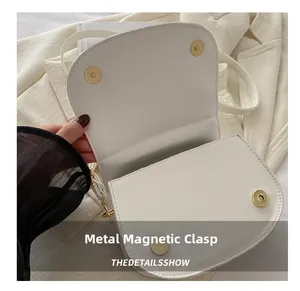 Dettaglio di una borsa a sella bianca con chiusure magnetiche dorate e ferramenta
