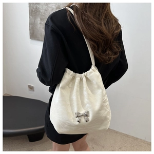 Detail of white pleated tote bag featuring a silver metal bow and drawstring closure