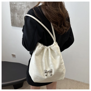 Detail of white pleated bucket bag with metallic bow and pearlescent texture finish