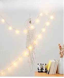 Detail of moon-shaped woven dreamcatcher with white feathers and warm LED string lights