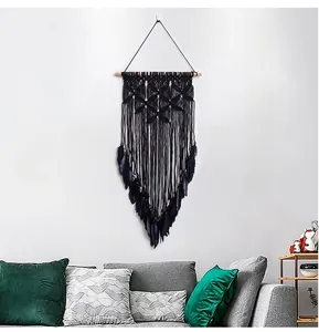 Detail of handmade black macrame wall hanging with feathers and a natural wood pole