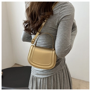 Detailed side view of a metallic gold saddle bag with U-shaped stitching on grey dress