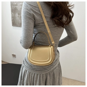 Moderna borsa a sella dorata con tracolla abbinata a un elegante abito grigio