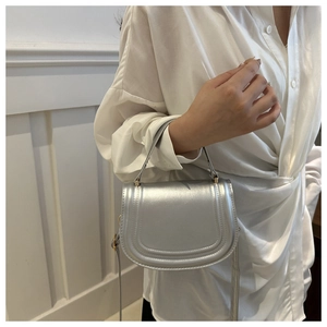 Detail view of a silver saddle bag with gold hardware held by a model in a minimal setting