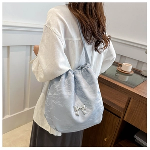 Detail of light blue satin bucket bag featuring a silver bow and drawstring closure