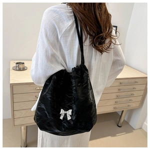 Detail of black drawstring bucket bag with silver butterfly buckle on soft pleated fabric