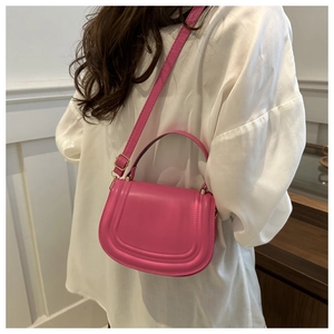 Borsa a sella in pelle rosa con tracolla regolabile indossata su modella in camicia bianca