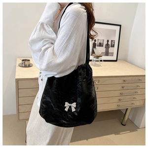 Detail of black pleated bucket bag with a silver butterfly buckle worn by a model