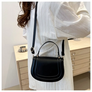 Minimalist black saddle bag for women worn over a white shirt in a cozy indoor setting