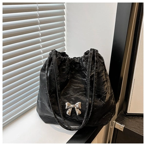 Detail of black pleated bucket bag with silver metal butterfly and drawstring closure