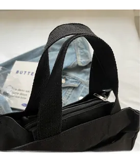 Close-up of black canvas tote bag featuring reinforced woven handles and metal zipper top