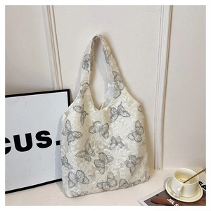Close-up of butterfly embroidery detail on white textured fabric tote bag