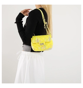 Detailed view of yellow quilted crossbody bag with gold twist lock and metal pendant charms