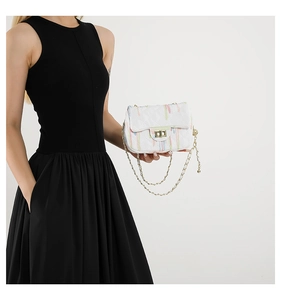 Close-up of white quilted crossbody bag with colorful trim and gold chain on black outfit