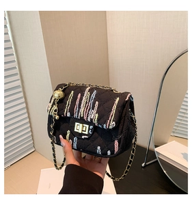 Detail of black quilted shoulder bag featuring colorful wavy embroidery and golden chain