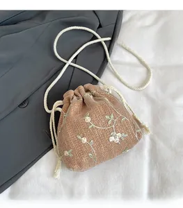 Dettaglio della borsa a secchiello intrecciata con ricami floreali e tracolla in corda