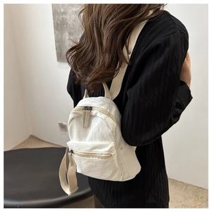 Detail of a cream nylon mini backpack showing the wrinkled texture and zipper pocket